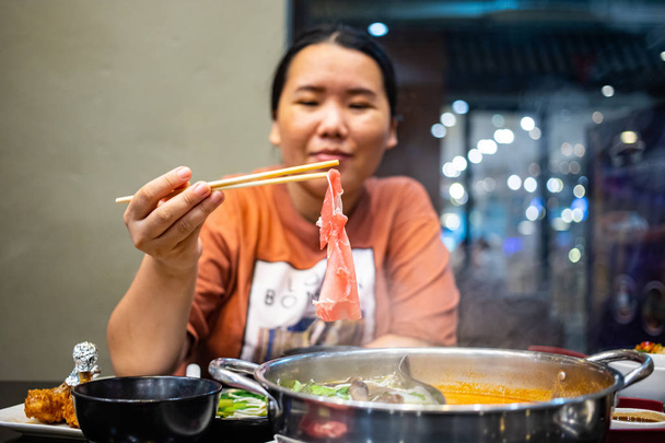 Счастливая пухленькая азиатка держит бамбуковые палочки с кусочком сырой нарезанной говядины
 - Фото, изображение
