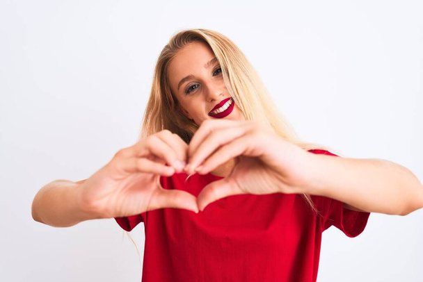 Jonge mooie vrouw draagt rode casual t-shirt staan over geïsoleerde witte achtergrond glimlachen in liefde tonen hart symbool en vorm met de handen. Romantisch concept. - Foto, afbeelding