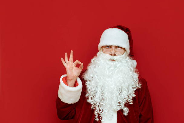 Santa Claus stands on a red background and shows his thumb gesture OK. Isolated. Santa and the gesture Okay. Christmas and New Year. Copyspace - Photo, Image