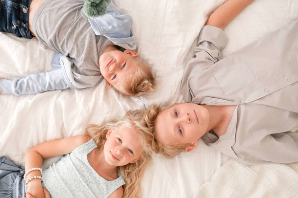 Three cheerful blonde kids are lying together on bed, looking at camera and smiling. Two boys and girl. Happy family, brothers and sister - Φωτογραφία, εικόνα