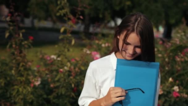 young girl, wearing glasses holding blue folder, posing for camera on street - Filmagem, Vídeo