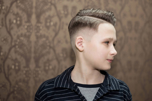 Corte de cabelo moderno elegante parte lateral retro com desbotamento médio com a separação de um menino da escola em uma barbearia em um fundo marrom
 - Foto, Imagem