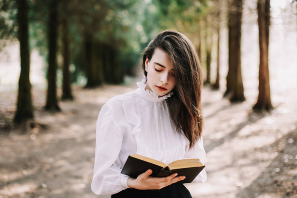 Young beautiful school or college girl reading a book in the park. Beautiful girl portrait. Romantic girl outdoors. - Fotó, kép