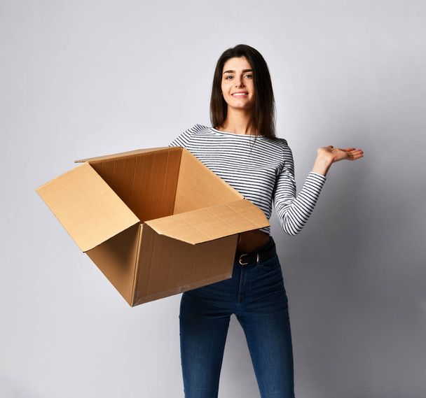 beautiful brunette woman standing on a light background with a moving cardboard box - Foto, Imagen