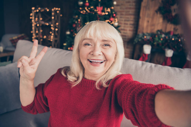 Self-portrait of her she nice attractive lovely cheerful cheery glad gray-haired granny spending winter December vacation showing v-sign at decorated industrial loft style interior house - Foto, Imagen