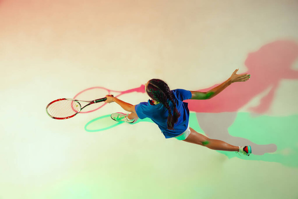 Молода жінка в синій сорочці грає в теніс у змішаному світлі. Молодь, гнучкість, влада та енергія
. - Фото, зображення