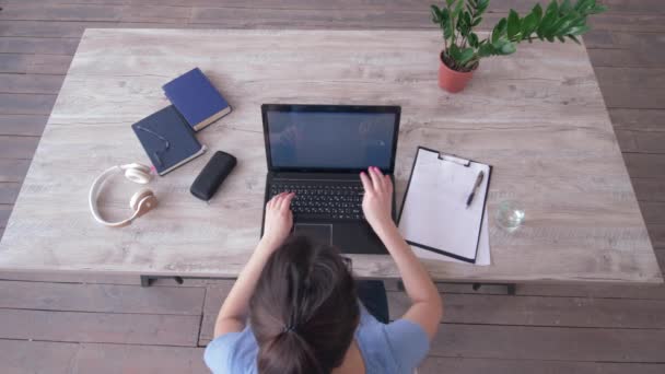 vista aérea de freelancer chica escribiendo texto en el teclado del ordenador portátil y escribe notas en portapapeles sentado en la mesa durante el estudio en línea
 - Metraje, vídeo