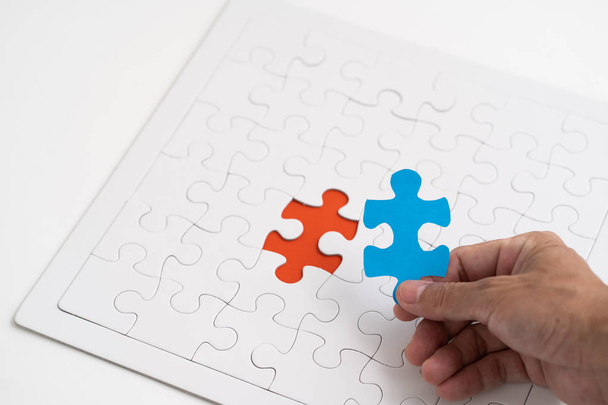 Hand holding blue piece jigsaw with red hold jigsaw background - 写真・画像