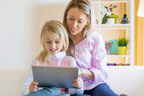 Blond vrolijk meisje met haar moeder met behulp van tablet computer samen - Foto, afbeelding