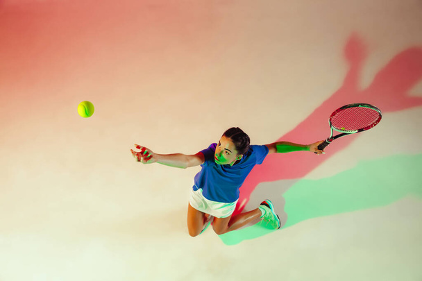 Mavi gömlekli genç bayan karışık ışıkta tenis oynuyor. Gençlik, esneklik, güç ve enerji. - Fotoğraf, Görsel