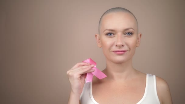 beautiful bald woman holds a pink ribbon in her hands. gentle pastel background. - Кадры, видео