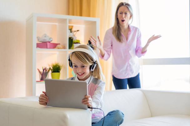 Woman is scolding her teenage daughter, girl is listening to music in headphones and ignoring her mom - Fotó, kép