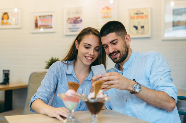 happy couple eating ice cream and using cellphone indoor - Фото, зображення