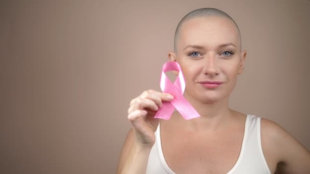 beautiful bald woman holds a pink ribbon in her hands. gentle pastel background. - Záběry, video