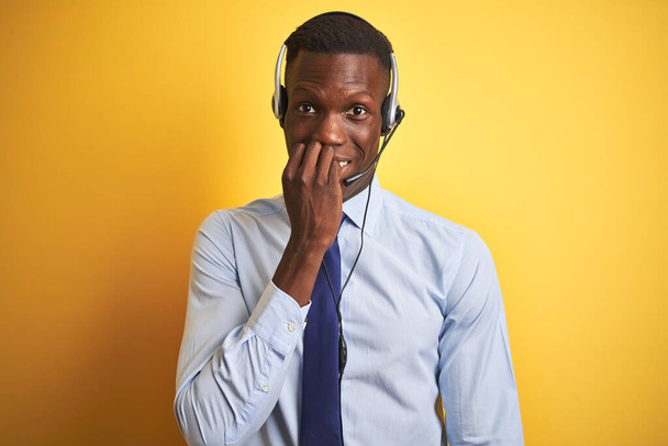 African american operator man working using headset over isolated yellow background looking stressed and nervous with hands on mouth biting nails. Anxiety problem. - Foto, Imagem