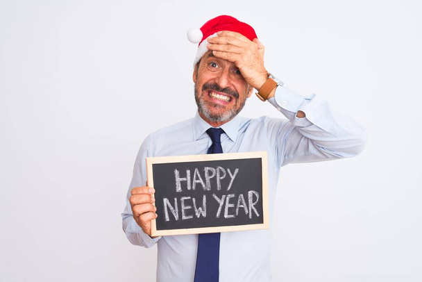 Senior businessman wearing christmas hat holding blackboard over isolated white background stressed with hand on head, shocked with shame and surprise face, angry and frustrated. Fear and upset for mistake. - Photo, Image
