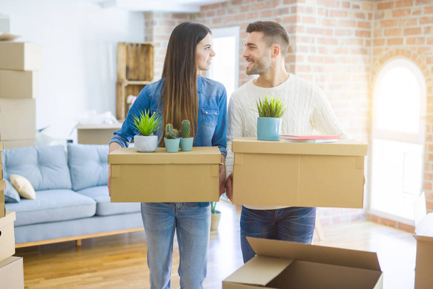 Молодая пара переезжает в новый дом, улыбаясь счастливо держа картонные коробки в новой квартире
 - Фото, изображение