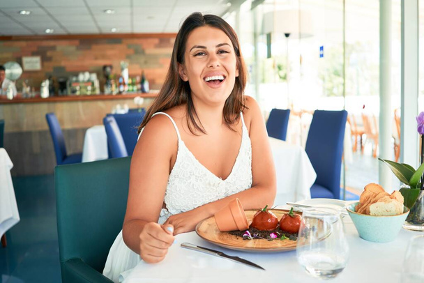 Young beautiful woman sitting at restaurant enjoying summer vacation eating delicious food - Foto, Imagem