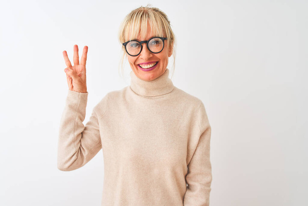 Mujer de mediana edad con jersey de cuello alto y gafas sobre fondo blanco aislado mostrando y señalando hacia arriba con los dedos número tres mientras sonríe confiado y feliz
. - Foto, Imagen