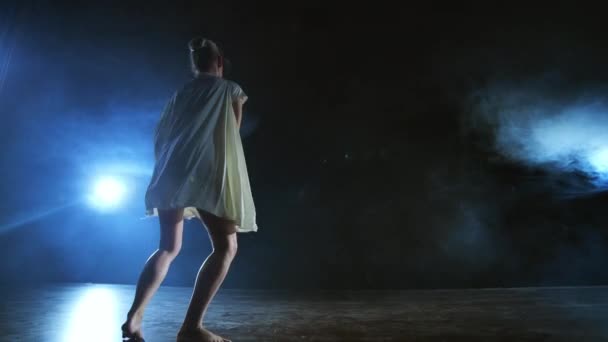 Молодая балерина босиком выпрыгивает на сцену и медленно движется в свободном белом платье
 - Кадры, видео
