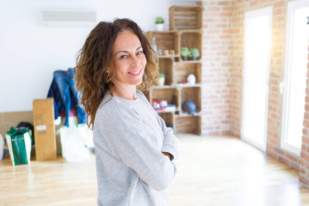 Beautiful middle age woman with curly hair smiling confident at new home, renovating and painting house - 写真・画像