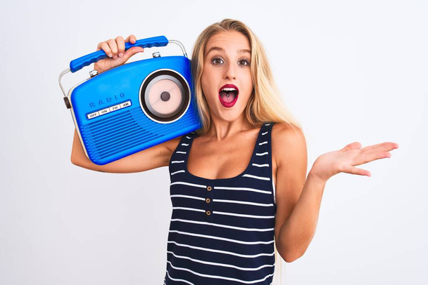 Young beautiful woman holding vintage radio standing over isolated white background very happy and excited, winner expression celebrating victory screaming with big smile and raised hands - Fotoğraf, Görsel