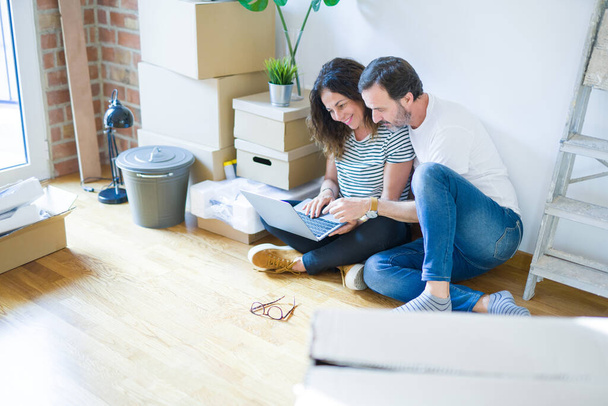 中年のシニアロマンチックなカップルは、周りのボックスとアパートの床に座って、新しい家に移動するための幸せな笑顔コンピュータのラップトップを使用して愛 - 写真・画像