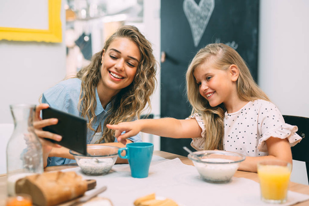 Having great time together. Mother and daughter using tablet while having breakfast at home.  - Foto, afbeelding