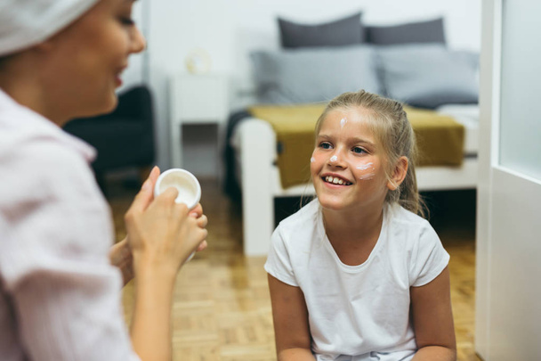 Mother applying face cream to daughter face at home - Foto, Imagem