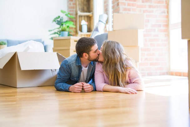 Young beautiful couple in love relaxing lying on the floor together with cardboard boxes around for moving to a new house - Fotoğraf, Görsel