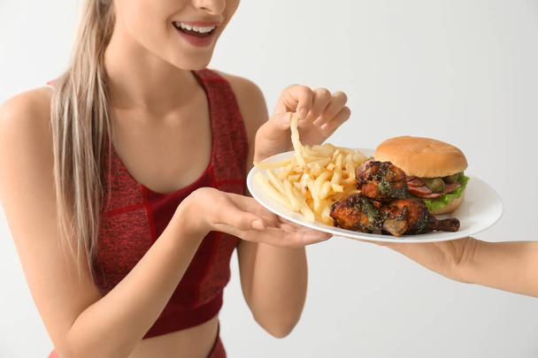 Sporty woman eating unhealthy food on light background. Diet concept - Photo, Image