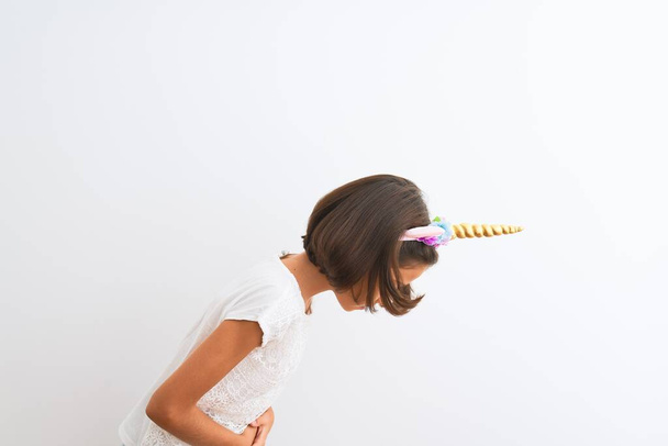 Beautiful child girl wearing unicorn diadem standing over isolated white background with hand on stomach because nausea, painful disease feeling unwell. Ache concept. - Foto, immagini