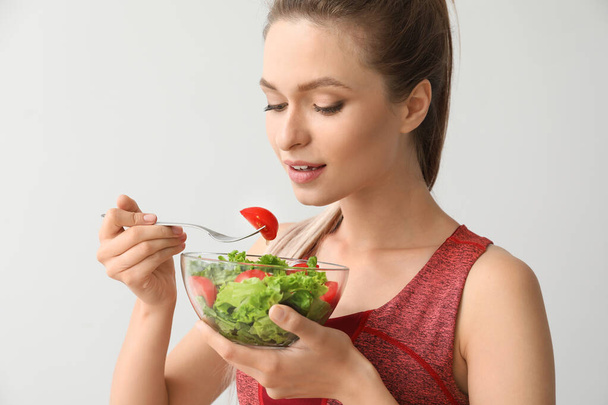 Sporty woman eating healthy vegetable salad on light background. Diet concept - Photo, Image