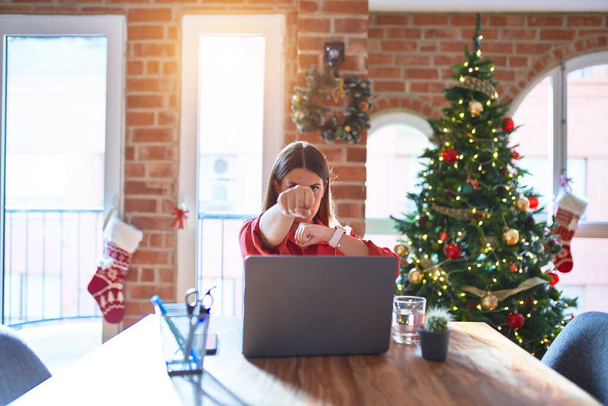 Beautiful woman sitting at the table working with laptop at home around christmas tree Punching fist to fight, aggressive and angry attack, threat and violence - 写真・画像