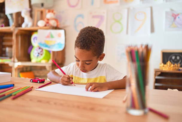 Bela criança africana americana sentado desenho usando papel e lápis na mesa no jardim de infância
 - Foto, Imagem