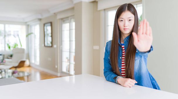 Young beautiful asian woman with long hair wearing denim jacket doing stop sing with palm of the hand. Warning expression with negative and serious gesture on the face. - Photo, Image