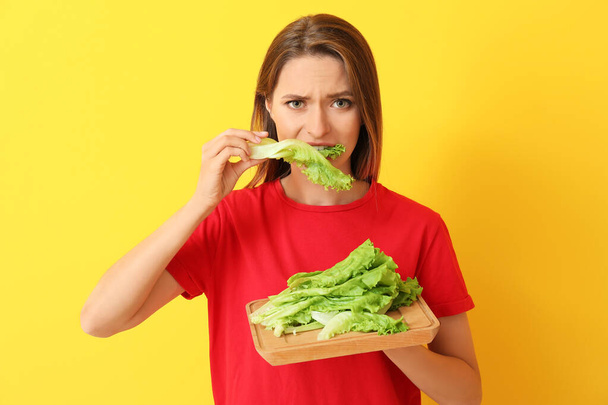 Stressed woman eating healthy lettuce on color background. Diet concept - Foto, Imagem