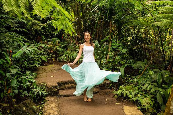Onnellinen nuori nainen tanssimassa kävelypolulla trooppisessa metsässä. Matkailuelämäntapa. Matka kohteeseen Ubud, Bali, Indonesia
. - Valokuva, kuva