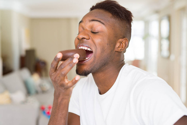 African american man eating  and enjoying a sweet chocolate donut - 写真・画像