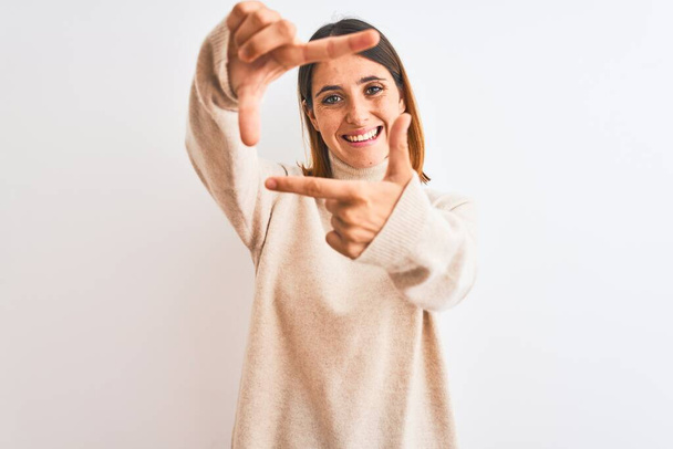 Mujer pelirroja hermosa con suéter de cuello alto de invierno sobre fondo aislado sonriendo haciendo marco con las manos y los dedos con la cara feliz. Concepto de creatividad y fotografía
. - Foto, Imagen