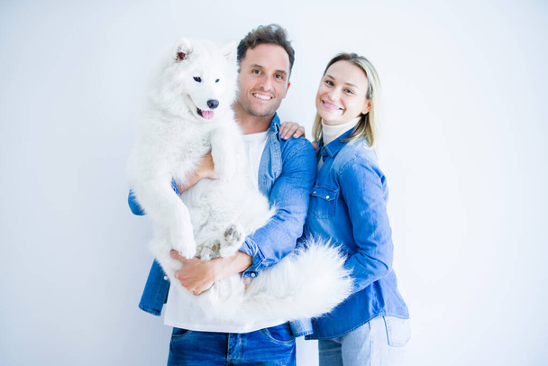 Young beautiful couple holding dog standing over isolated white background - Foto, immagini