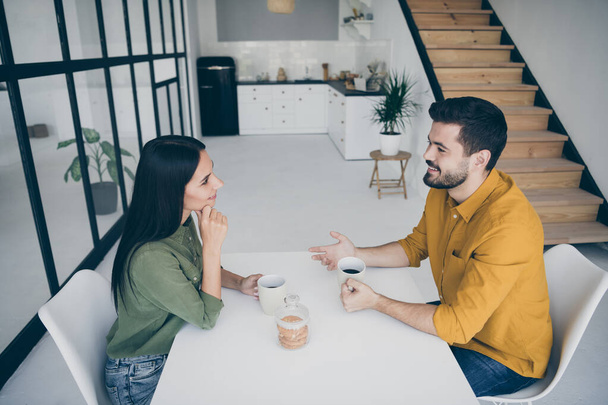 Profile photo of handsome guy and his pretty lady drinking hot beverage sitting chairs opposite in stylish interior light kitchen room indoors wear casual clothes - 写真・画像