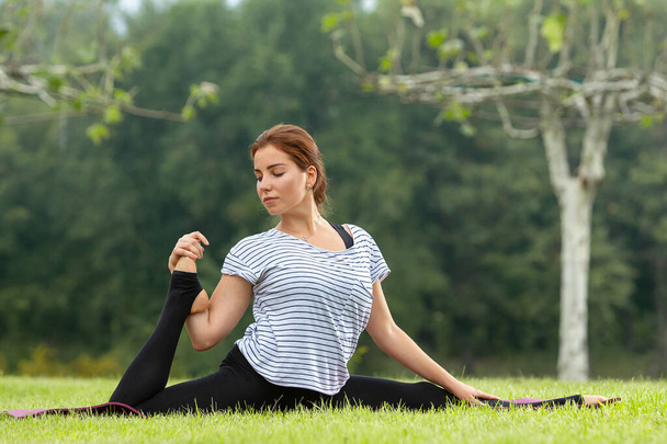Young beautiful woman doing yoga exercise in green park. Healthy lifestyle and fitness concept. - 写真・画像