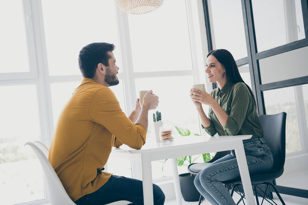 Profile photo of handsome guy and his pretty lady looking tender eyes drinking hot beverage sitting chairs opposite in stylish interior light cafeteria indoors wear casual clothes - Фото, изображение