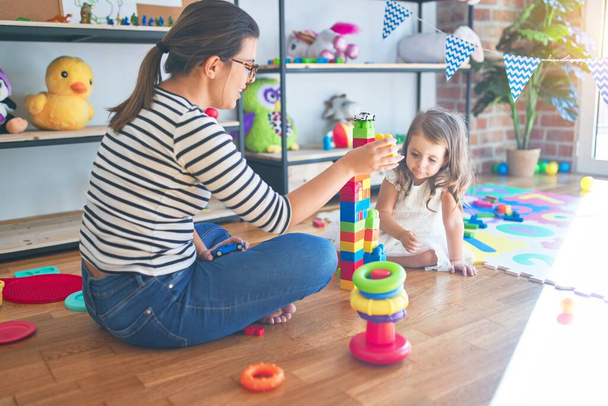 Hermosa maestra mujer y niño pequeño jugando con bloques de construcción alrededor de un montón de juguetes en el jardín de infantes
 - Foto, imagen