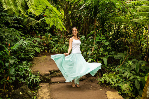 Gelukkige jonge vrouw dansend op wandelpad in tropisch bos. Reizen levensstijl. Reis naar Ubud, Bali, Indonesië. - Foto, afbeelding