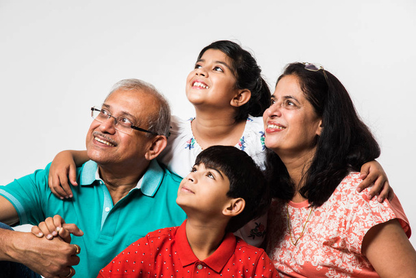 Индийские дети с бабушкой и дедушкой улыбаются, сидя на белом фоне в помещении, избирательный фокус
 - Фото, изображение
