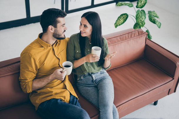 Photo of funny guy and lady having fun best weekend sharing fresh news drinking hot beverage student life sit sofa in modern interior trendy flat indoors wear casual clothes - Fotografie, Obrázek