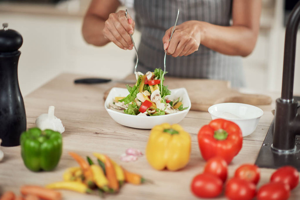 close-up van gemengde ras vrouw in schort mengen groenten in kom  - Foto, afbeelding