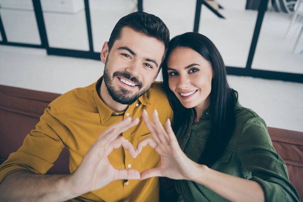 Close up photo of handsome guy and his wife lady moving to first flat as married people showing heart figure with arms in modern flat indoors wear casual clothes - Photo, image